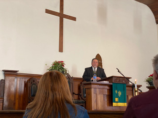 A picture of the pastor standing and speaking with the audience